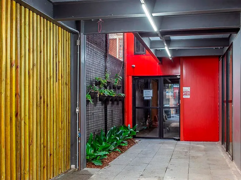 Corredor de entrada da Galeria Osiris com ripado de madeira, jardim vertical e parede vermelha
