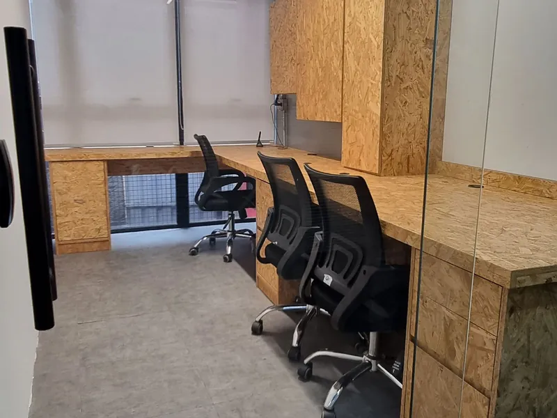 Sala privada com bancada contínua em madeira, armários superiores e três cadeiras ergonômicas