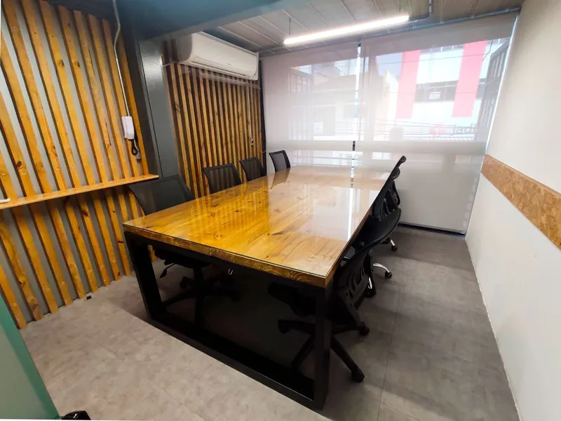 Sala de reunião com mesa de madeira envernizada, cadeiras pretas, ar-condicionado e persiana